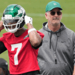 Geno Smith puts on his Jets helmet while offensive coordinator Frank Reich watches during minicamp practice.