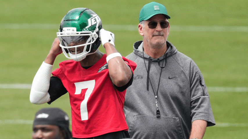 Geno Smith puts on his Jets helmet while offensive coordinator Frank Reich watches during minicamp practice.
