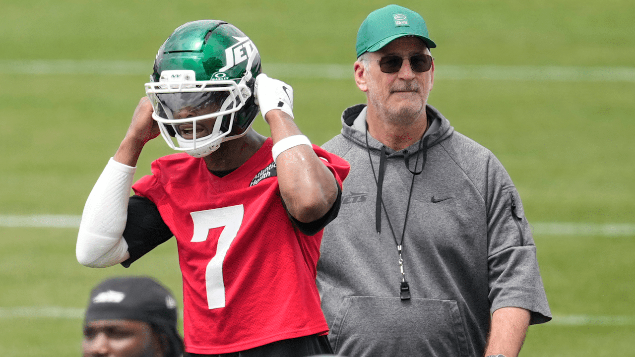 Geno Smith puts on his Jets helmet while offensive coordinator Frank Reich watches during minicamp practice.